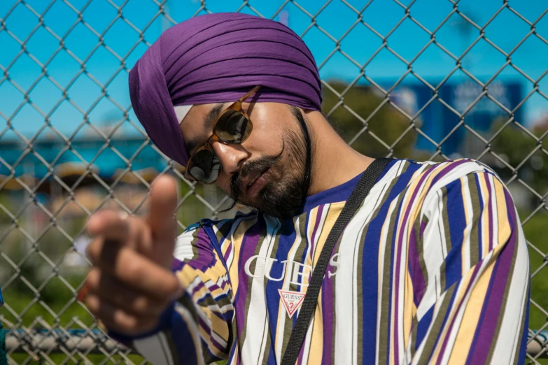a man with sunglasses is wearing a purple turban and points at his finger
