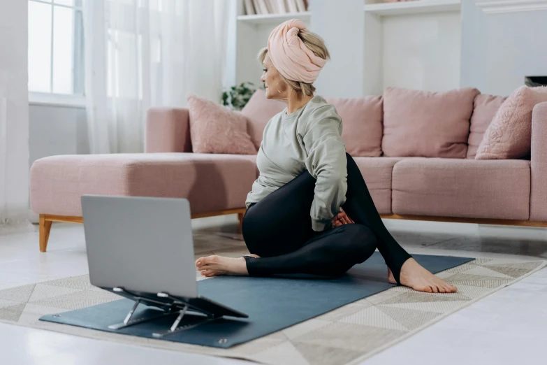 a woman sitting on a yoga mat in front of a laptop, happening, half turned around, sitting in a lounge, profile image