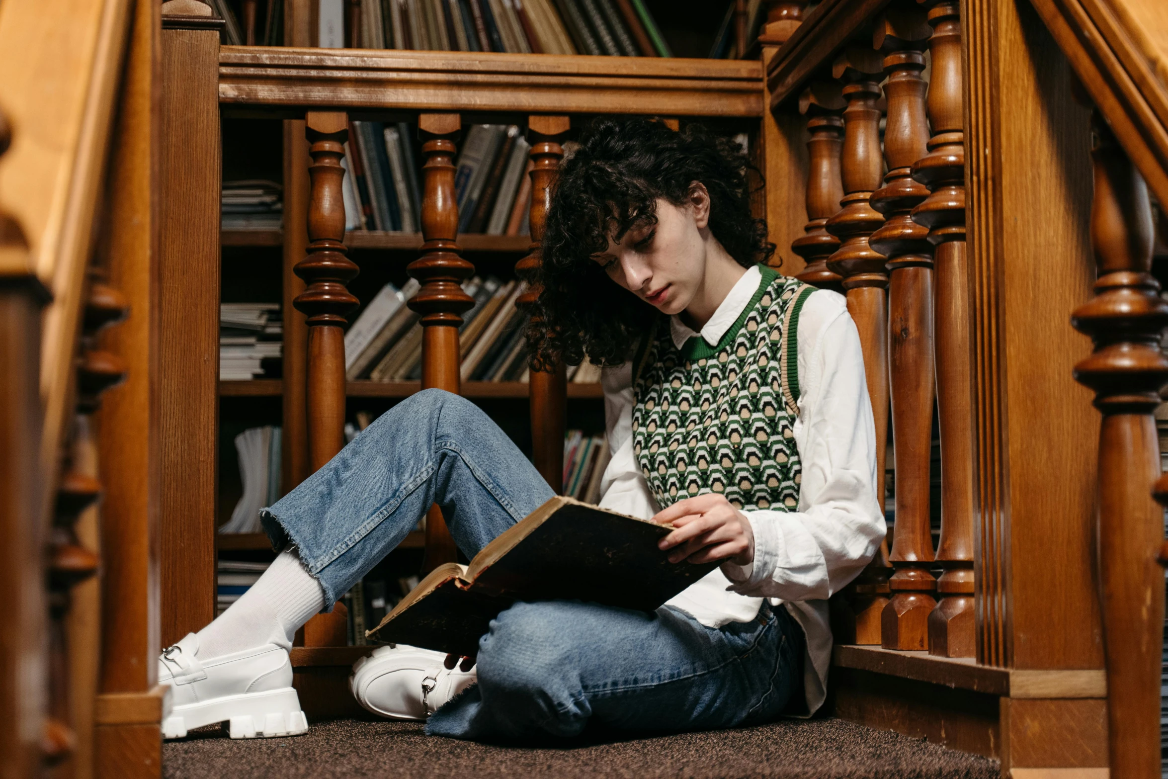 a woman sitting on the floor reading a book, trending on pexels, renaissance, finn wolfhard, academic clothing, in a library, androgynous male
