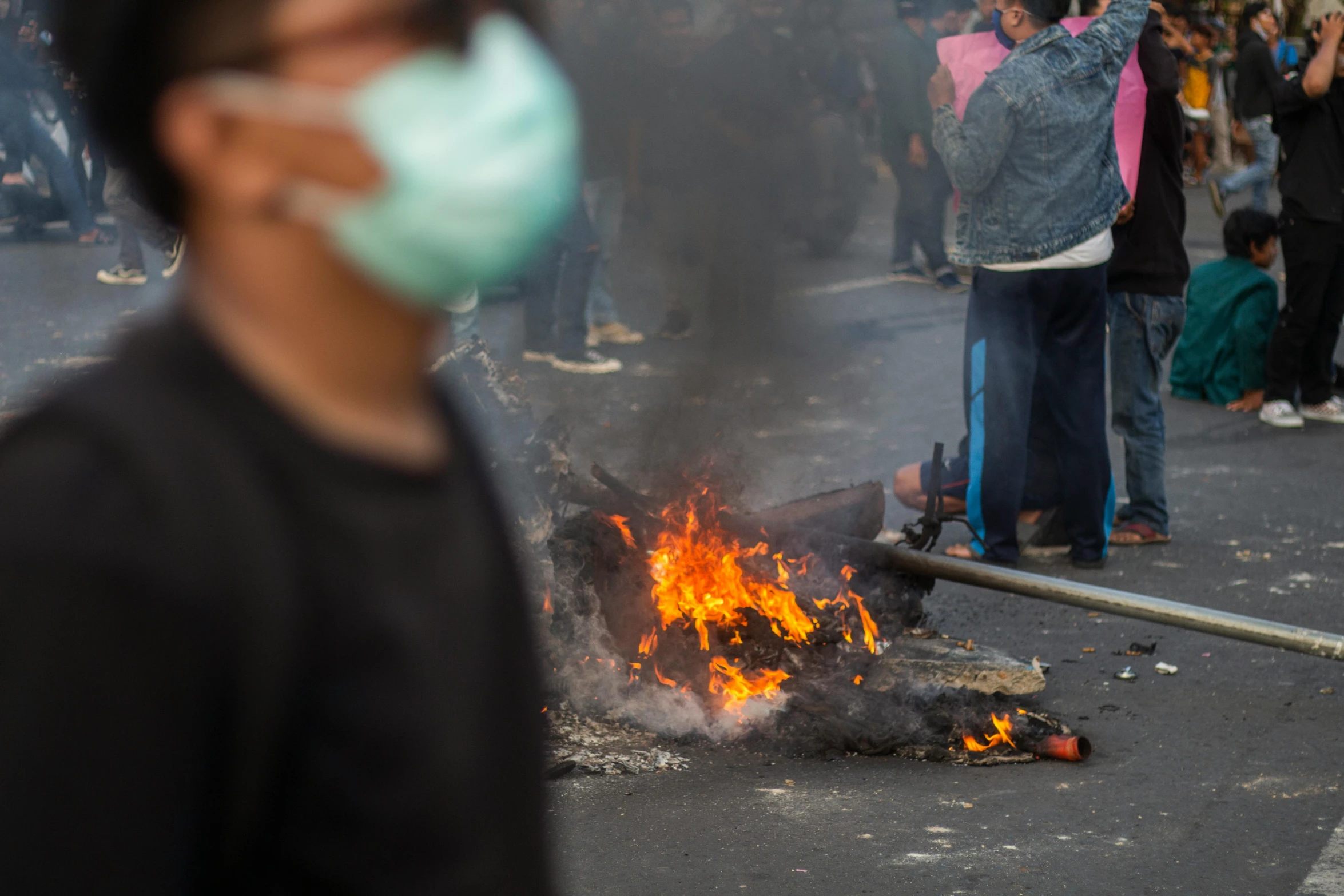 a man with a face mask on stands in front of a burning object