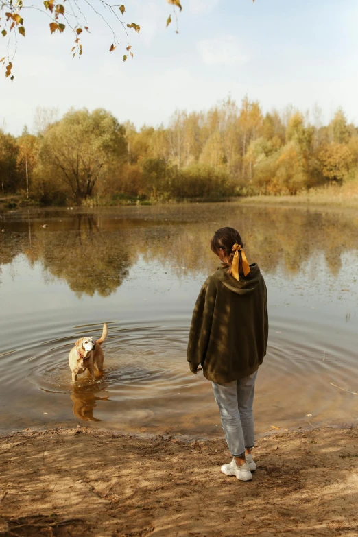 a woman standing in the water next to a dog, by Grytė Pintukaitė, unsplash, conceptual art, autumn season, teen boy, ponds, tan