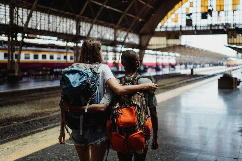 a couple of people standing next to each other at a train station, pexels contest winner, a backpack, best friends, 🚿🗝📝