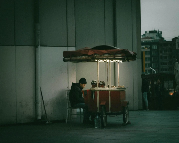 a person sitting at a table under an umbrella, inspired by Elsa Bleda, unsplash contest winner, cyberpunk homeless, cart, square, food stall