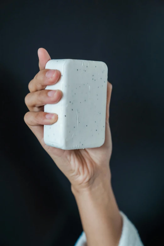 a hand holding a white square soap bar