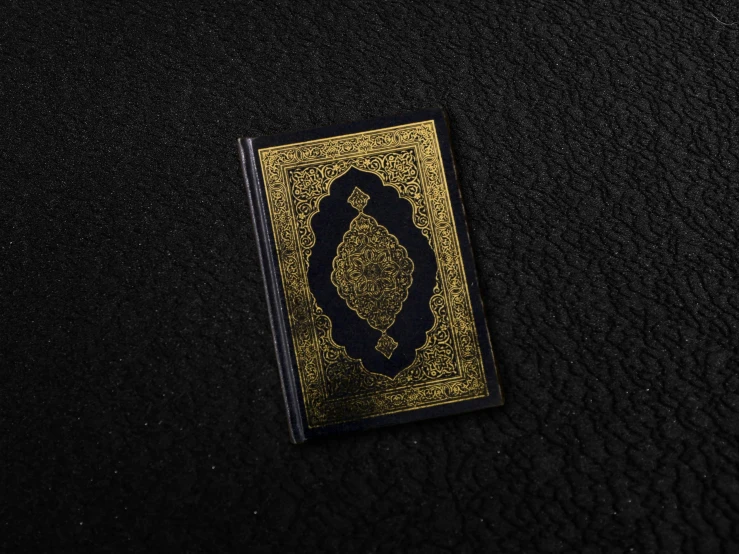 a black and gold book laying on a black surface, hurufiyya, small, mobile wallpaper, islamic, detailed product image