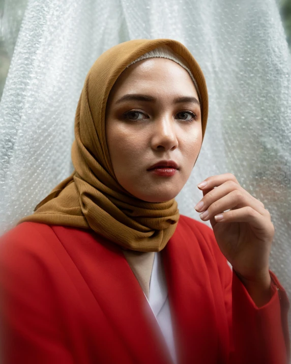 a woman wearing a hijab standing in front of a curtain, inspired by Sasha Putrya, trending on pexels, wearing red jacket, non binary model, serious business, wearing a brown