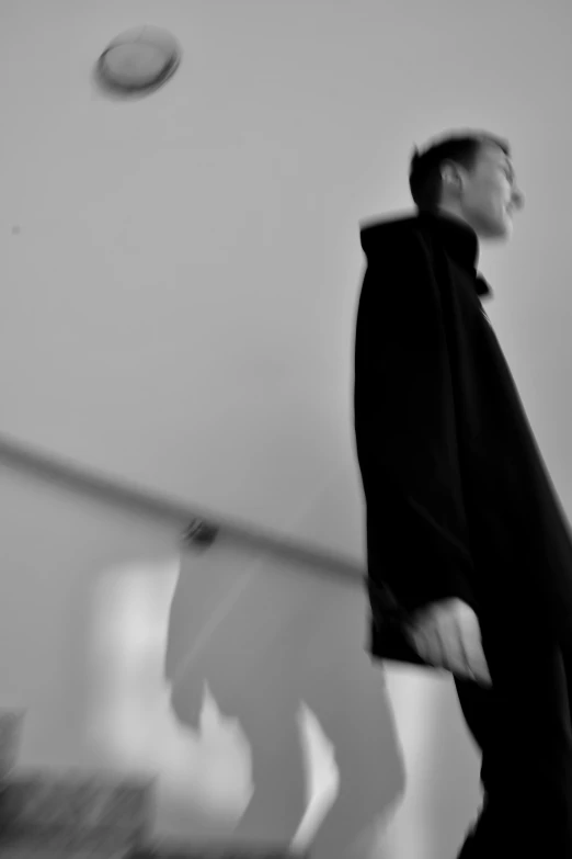 a black and white photo of a man throwing a frisbee, a black and white photo, unsplash, conceptual art, wearing black overcoat, catwalk, wong kar wai, blurred face