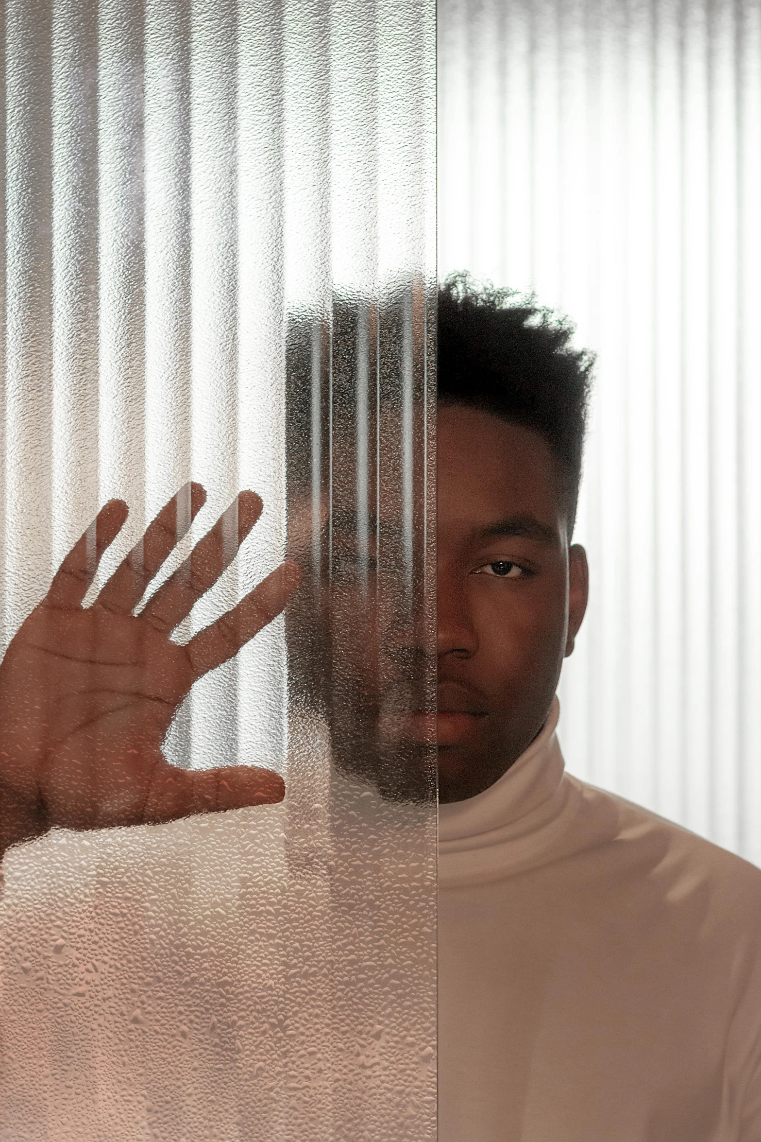 man in white turtleneck shirt with hand out looking in the mirror