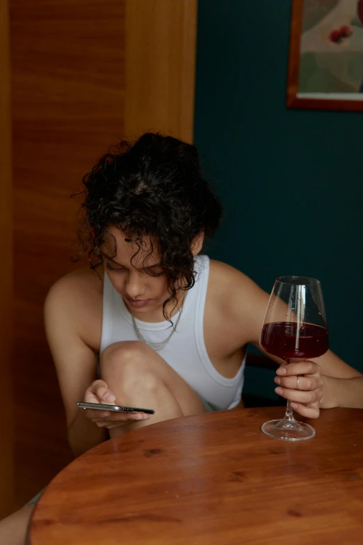 a woman sitting at a table with a glass of wine, inspired by Nan Goldin, trending on pexels, renaissance, checking her phone, queer woman, gaming, hotel room