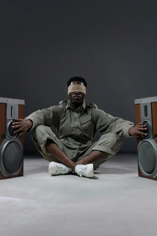 a man sitting on the floor in front of speakers, by Morris Kestelman, trending on reddit, afrofuturism, studio shot, blindfold, ( ( theatrical ) ), surgeon