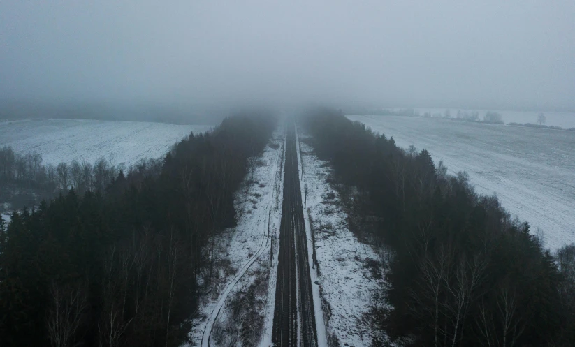 a train traveling through a rural countryside covered in snow, an album cover, by Adam Marczyński, pexels contest winner, under a gray foggy sky, drone point of view, infinitely long corridors, distant forest horizon