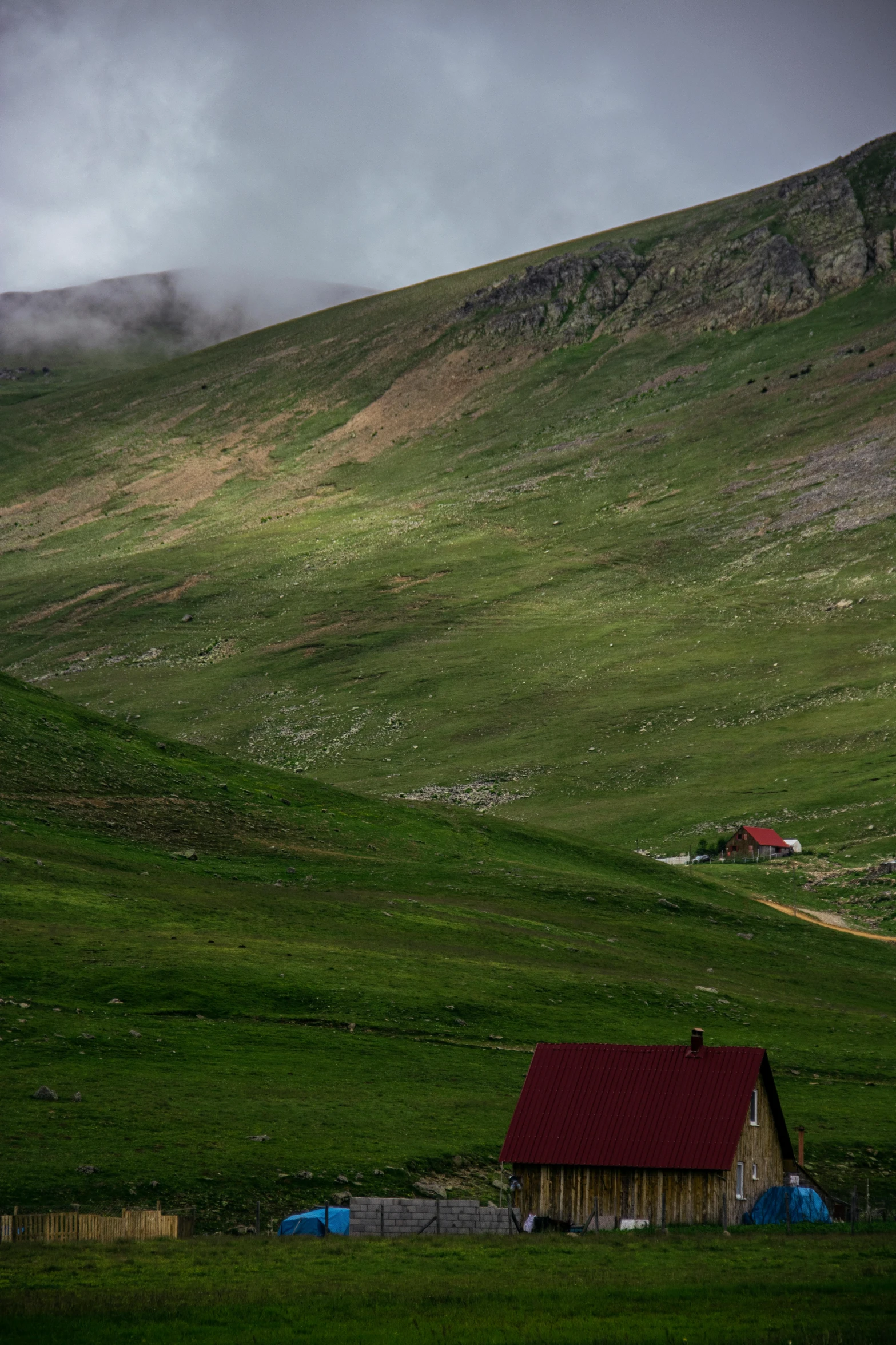 a small house sitting on top of a lush green hillside, by Muggur, les nabis, green and red tones, tundra, grey skies, alp