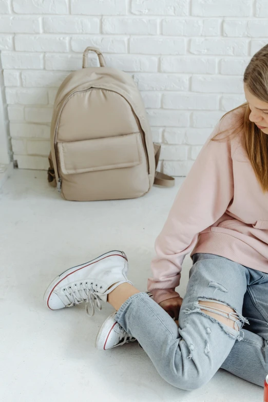 a woman sitting on the floor reading a book, trending on pexels, happening, wearing strawberry backpack, wearing a pastel pink hoodie, ripped up white garment, blue jeans and grey sneakers