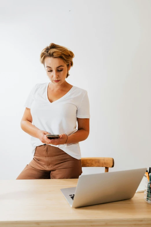 a woman sitting at a table looking at her cell phone, trending on pexels, renaissance, standing on a desk, wearing tight shirt, minimalist home office, hovering indecision