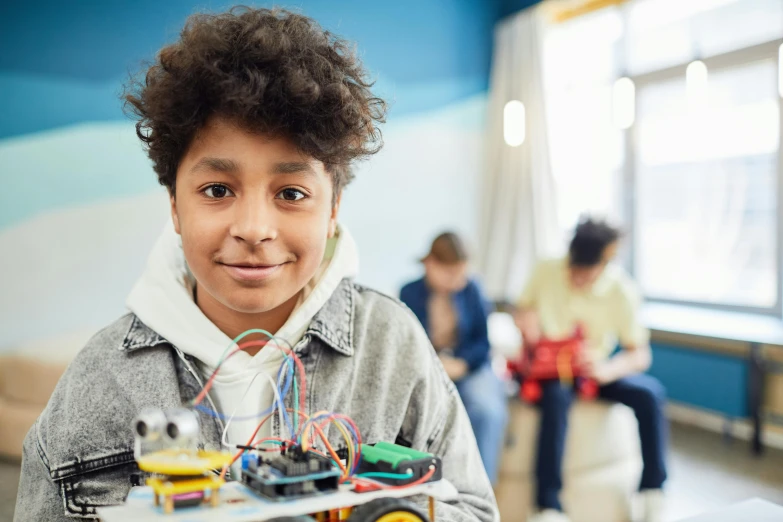 a close up of a person holding a robot, in a school classroom, looking confident, black teenage boy, complicated circuits and wires