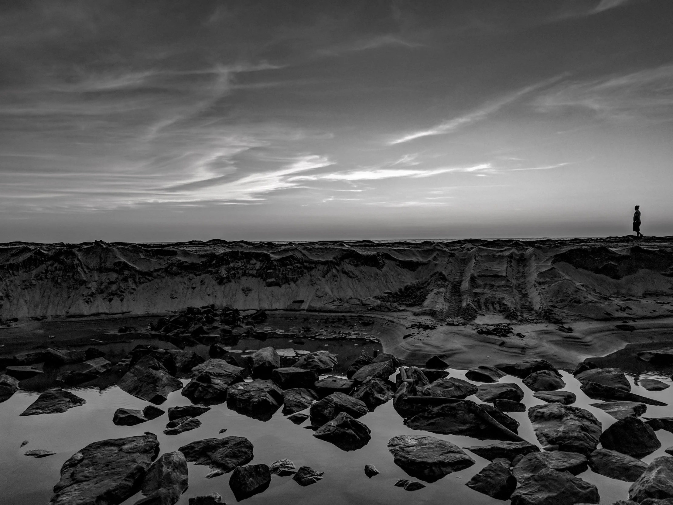 a man standing on top of a rocky beach, a black and white photo, by Jan Kupecký, martian landscape, dusk, pools of water, black white