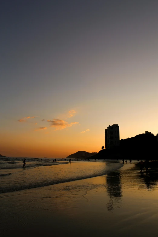 a group of people standing on top of a beach next to the ocean, golden towers, which shows a beach at sunset, favela, lisa brawn