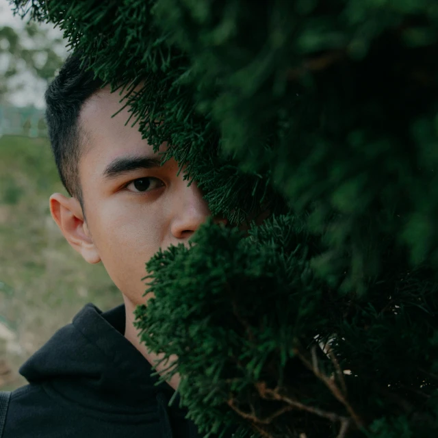 a young man standing in front of a tree, inspired by Yu Zhiding, pexels contest winner, hiding behind obstacles, asian face, headshot profile picture, spying