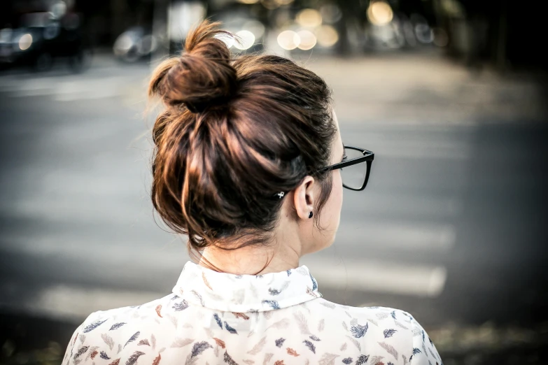 a woman with glasses standing in the middle of a street, pexels contest winner, hair tied up in a bun, view from back, bedhead, chestnut hair