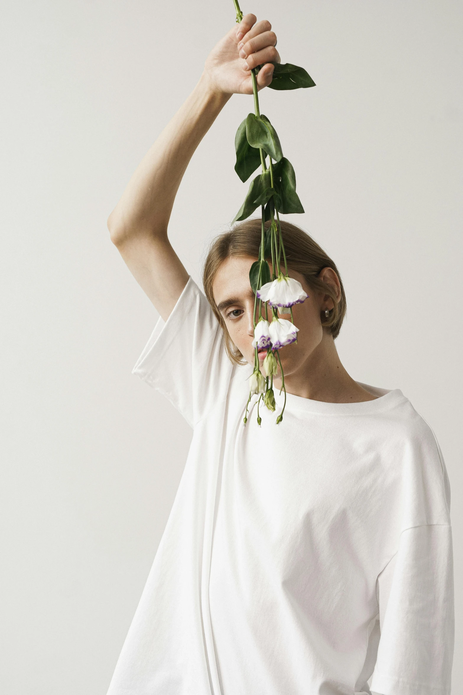 a woman holding a flower in front of her face, an album cover, unsplash, aestheticism, dressed in a white t-shirt, showstudio, ignant, hanging