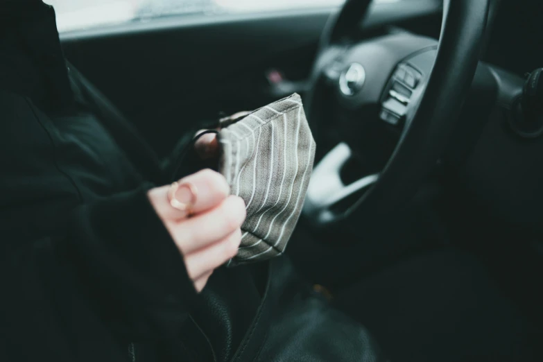 a person sitting in the driver's seat of a car, by Emma Andijewska, pexels contest winner, black bandana mask, holding a stuff, no face mask, square