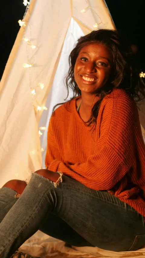 a woman sitting in front of a teepee at night, by Dorothy Bradford, pexels, hurufiyya, smiling young woman, studio!! portrait lighting, brown skin, autumn season