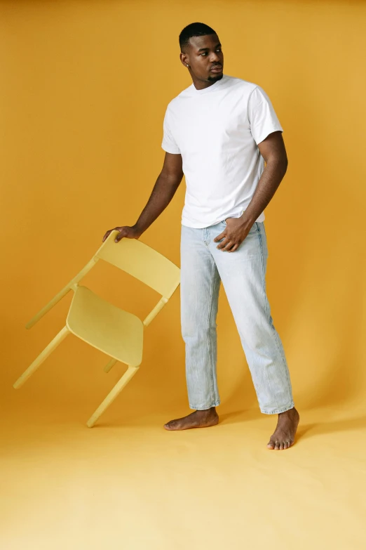 a black man holds a chair up against a yellow background