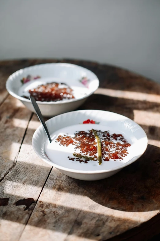 two bowls of food sitting on top of a wooden table, inspired by Modest Urgell, sugar sprinkled, morning detail, enamel, syrup