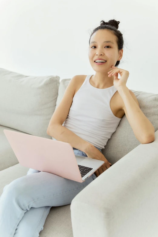 a woman sitting on a couch with a laptop, inspired by helen huang, pexels contest winner, white and pink, welcoming smile, slightly minimal, asian male