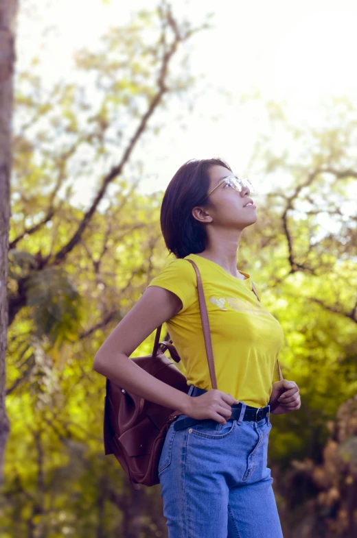 a woman standing next to a tree in a forest, pexels contest winner, happening, wearing a modern yellow tshirt, with a backpack, sunny sky, indian girl with brown skin