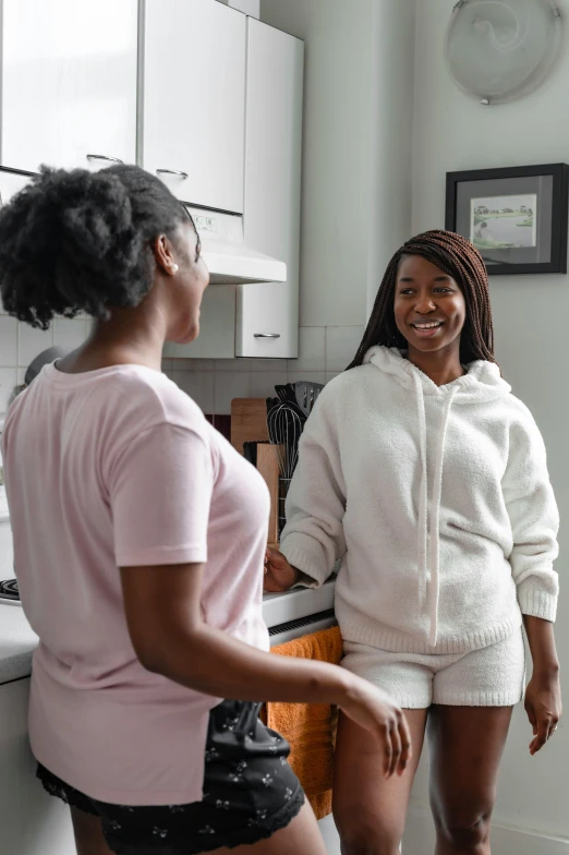 a couple of women standing next to each other in a kitchen, happening, smiling at each other, african canadian, wearing white pajamas, profile image