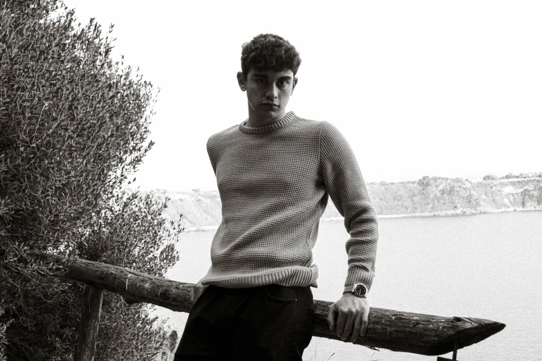 a black and white photo of a man holding a skateboard, a black and white photo, inspired by Luca Zontini, brown sweater, cartier, in a scenic background, riccardo scamarcio