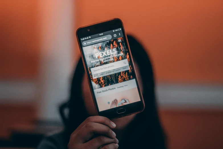 a person holding a cell phone in their hand, a picture, trending on pexels, pixel art, dark grey and orange colours, everything fits on the screen, thumbnail, over-the-shoulder shot