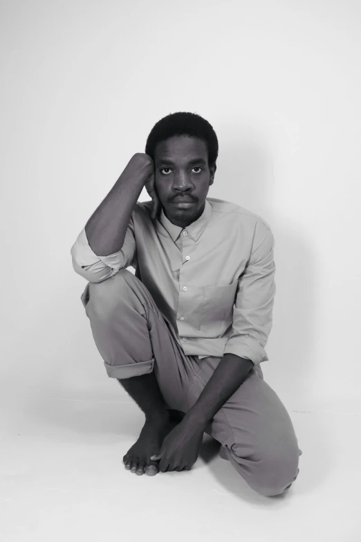 a black and white photo of a man sitting on the ground, maria borges, on a pale background, confident pose, riyahd cassiem