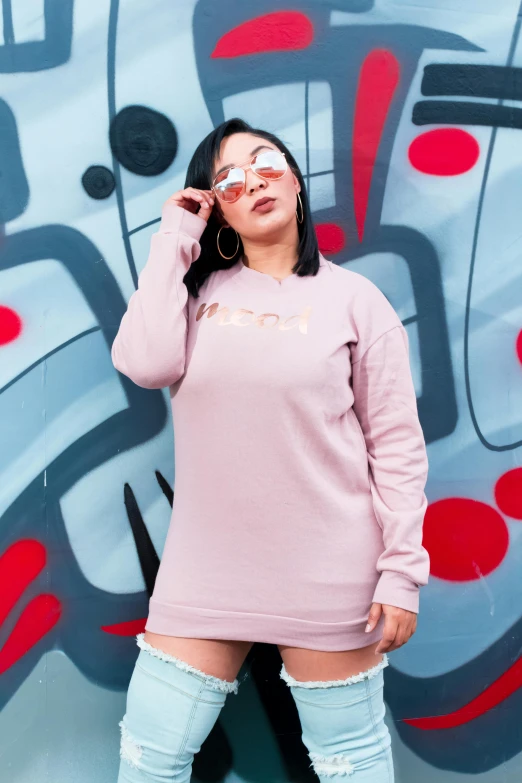 a woman standing in front of a graffiti wall, a cartoon, inspired by Gina Pellón, trending on pexels, lyco art, wearing casual sweater, pastel pink skin tone, meow, wearing a pink dress