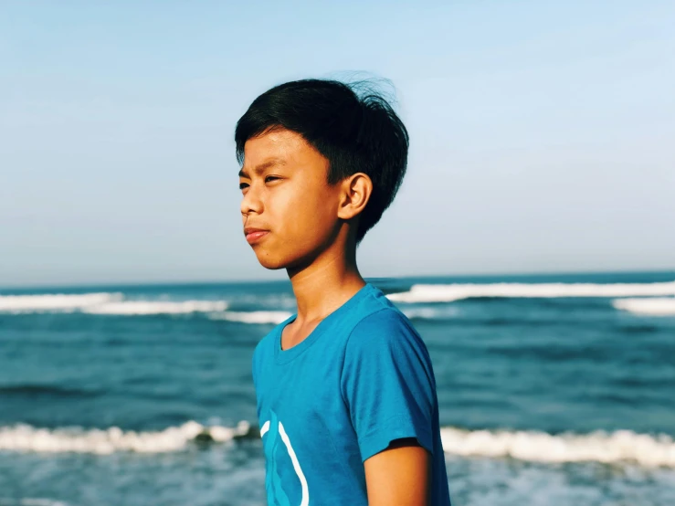 a young boy standing on top of a beach next to the ocean, pexels contest winner, sumatraism, halfbody headshot, avatar image, profile pic, young cute wan asian face