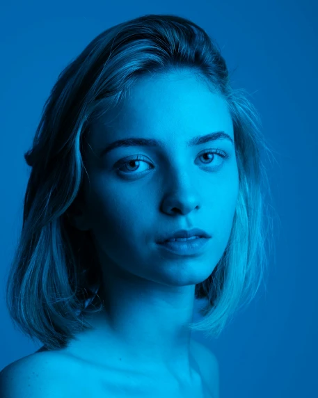 a woman standing in front of a blue background, a character portrait, inspired by Elsa Bleda, unsplash contest winner, antipodeans, kiko mizuhara, young blonde woman, dark. studio lighting, 18 years old