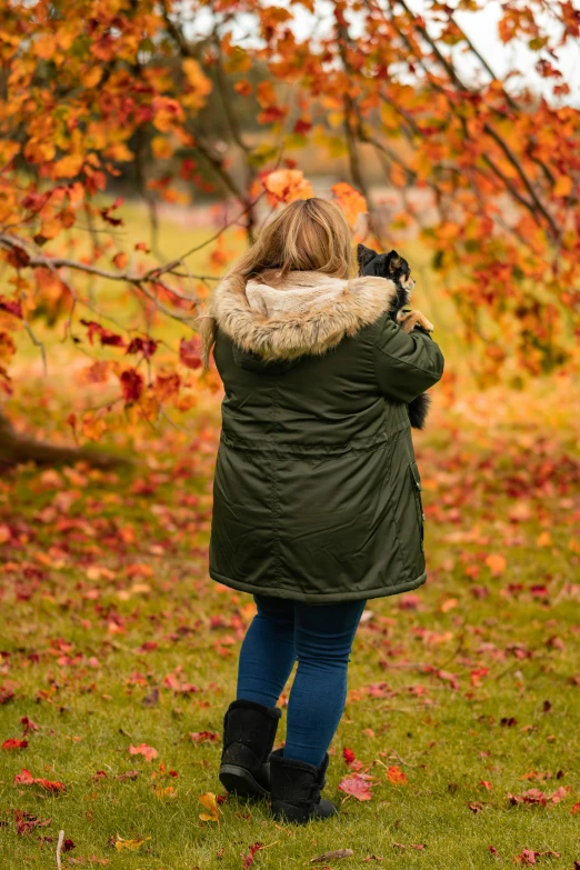 a woman taking a picture of a tree with her camera, black and orange coat, shot on 1 5 0 mm, autumn colours, f / 8