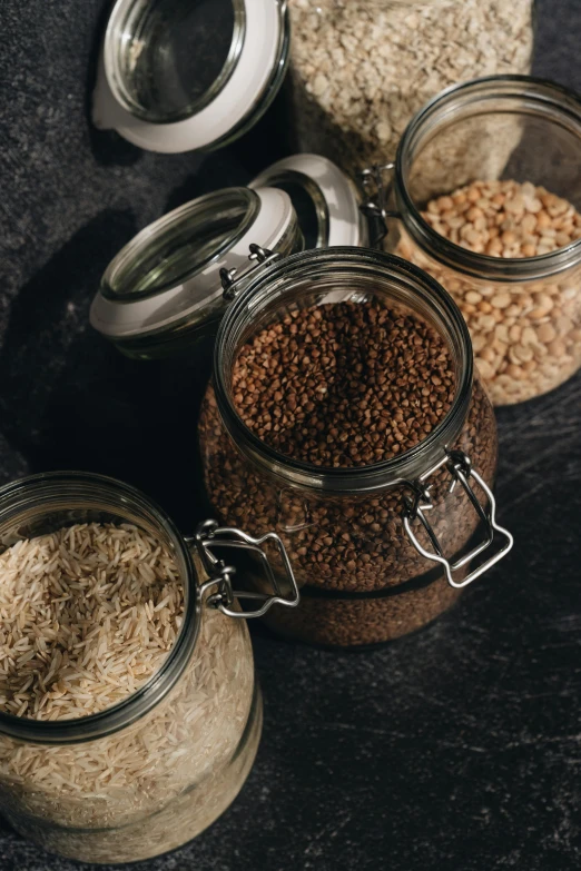 a table topped with jars filled with different types of food, a still life, pexels, mineral grains, brown, with a black background, detailed product image