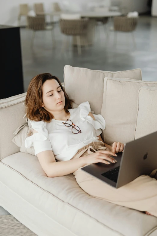 a woman sitting on a couch using a laptop, trending on pexels, renaissance, sleepy, wearing business casual dress, lazy eye, white