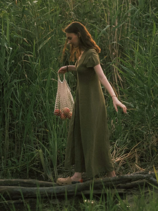 a woman standing on a log in a field, a picture, inspired by Elsa Bleda, unsplash, renaissance, olive green, holding a baguette, in a swamp, wearing dress