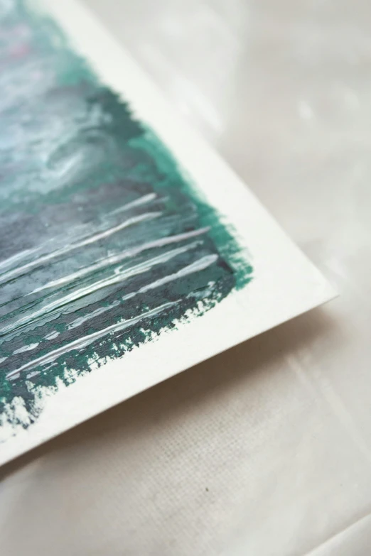 a piece of art sitting on top of a table, inspired by Hu Zao, unsplash, modern european ink painting, cut paper texture, close - up photograph, teal paper, on white paper