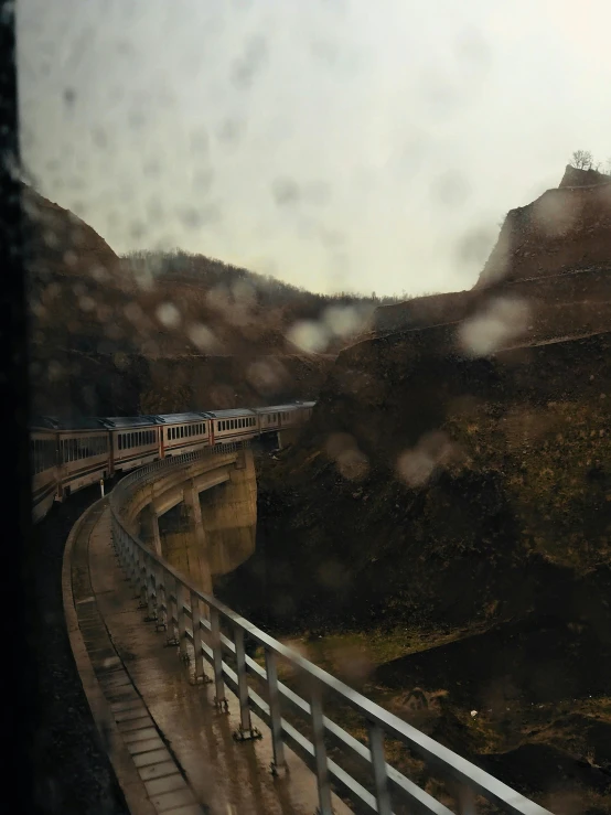 a view of a train going over a bridge, pexels contest winner, regionalism, raining outside the window, gorge in the mountain, thumbnail, low quality photo