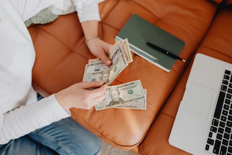 a woman sitting on a couch holding a bunch of money, by Daniel Lieske, pexels contest winner, couch desk, sitting at his desk, holding a 🛡 and an 🪓, carson ellis