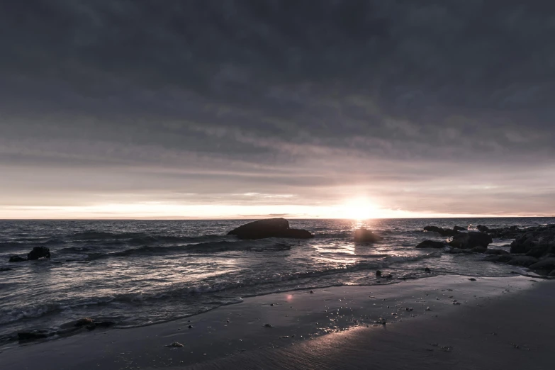 a rocky beach under a cloudy sky with a rock in the ocean