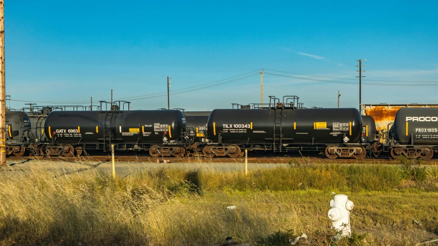 a train traveling down train tracks next to a field, by Sven Erixson, shutterstock, graffiti, propane tanks, black and yellow color scheme, high resolution photo, trading depots