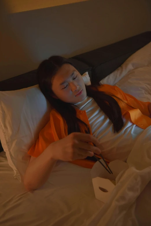 a woman laying in bed using a cell phone, inspired by Fei Danxu, video art, orange, capsule hotel, taken with sony alpha 9, sleepy expression