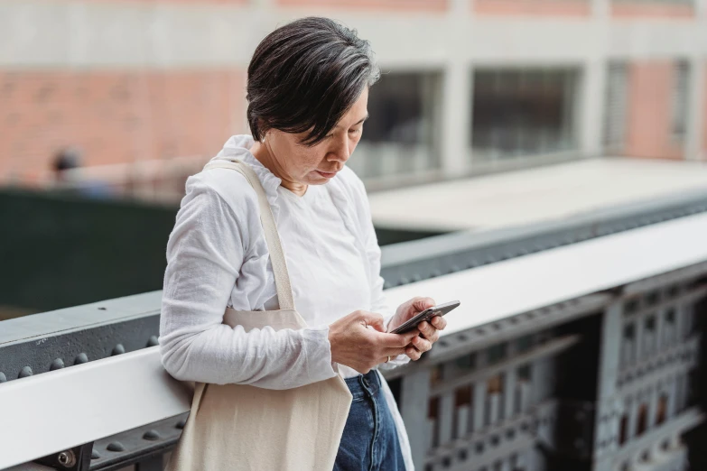 a woman standing on a bridge looking at her cell phone, trending on pexels, middle - age, avatar image, woman with black hair, wearing a linen shirt