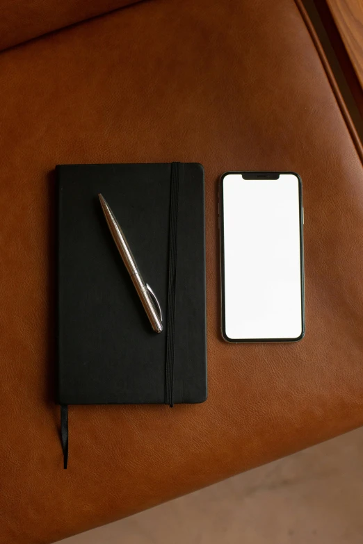 a notepad sitting on top of a brown chair next to a cell phone, all black matte product, fountain pen, taken on iphone 14 pro, detailed product image