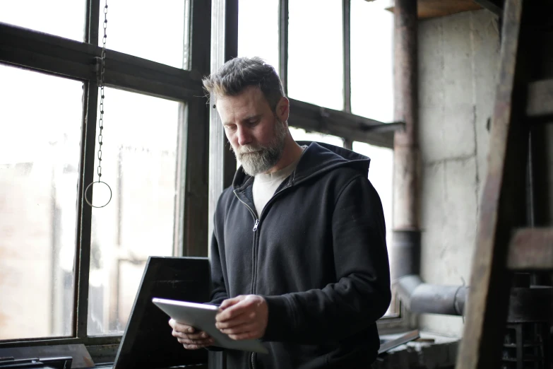 a man standing in front of a window holding a tablet, by Joseph Severn, pexels contest winner, blacksmith product design, lachlan bailey, gray beard, 2 5 6 x 2 5 6 pixels